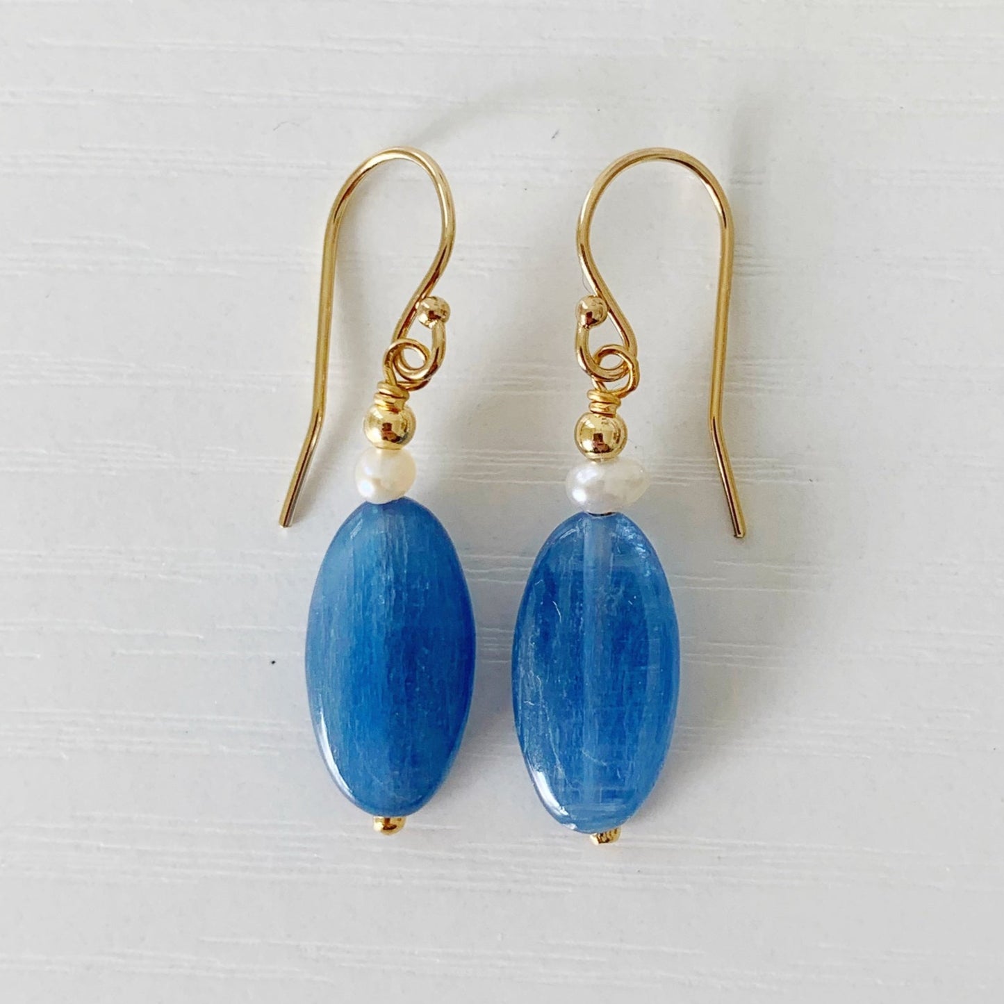 The Brewster Earrings by mermaids and madeleines are designed with blue kyanite elongated oval beads, petite freshwater pearls and 14k gold filled beads and findings. This is a drop style earring and this pair is photographed on a white surface