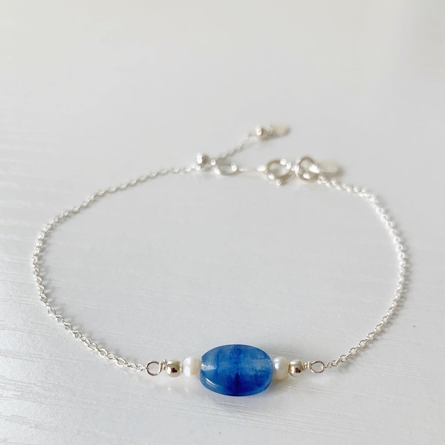 the brewster adjustable bracelet by mermaids and madeleines is an adjustable chain bracelet with medium blue kyanite small oval gem at the center with freshwater pearls on either side with sterling silver chain, beads, findings and slide bead clasp