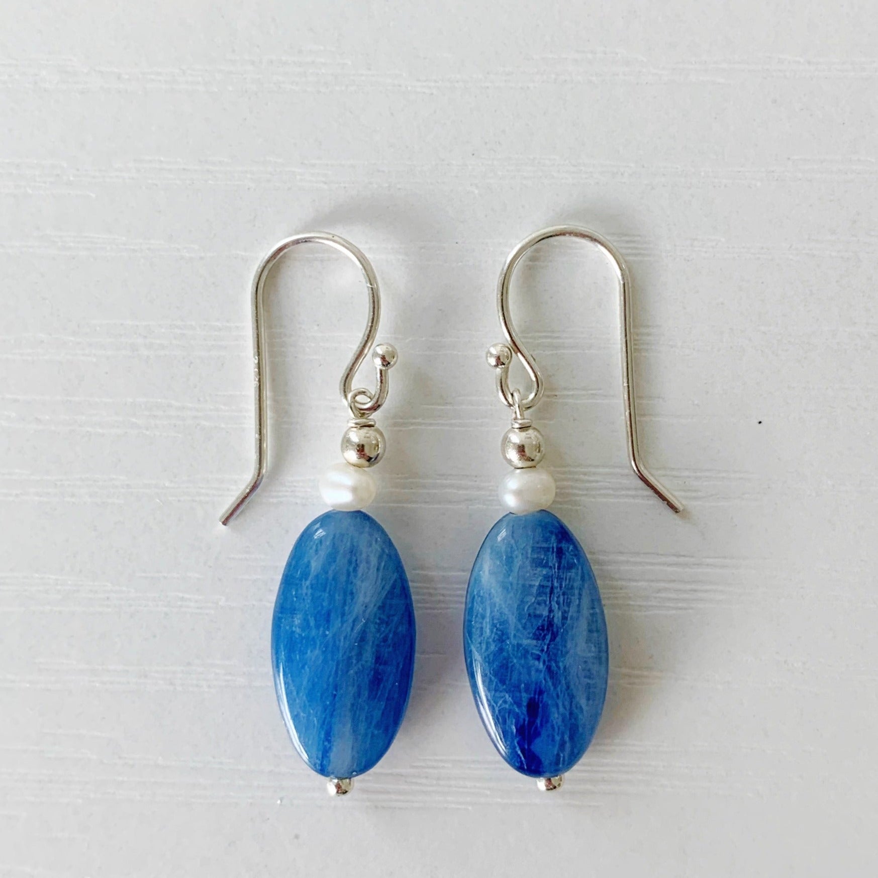 The Brewster earrings by mermaids and madeleines are elongated blue kyanite oval drop earrings with petite freshwater pearls and sterling silver beads with findings. this pair is photographed on a white background