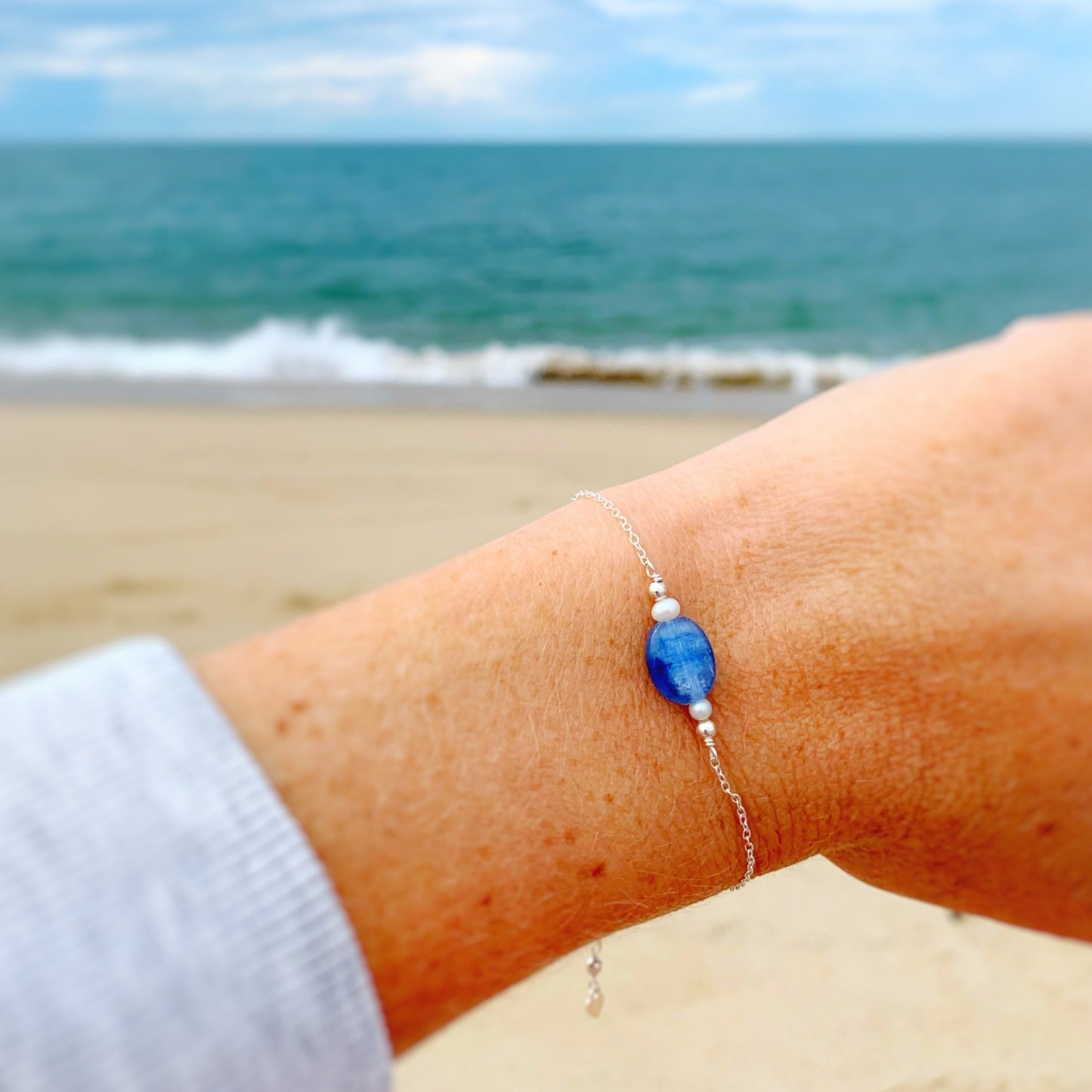 this image is of a close up view of the brewster bracelet on a wrist. the background in this picture is a soft and blurry beach scene