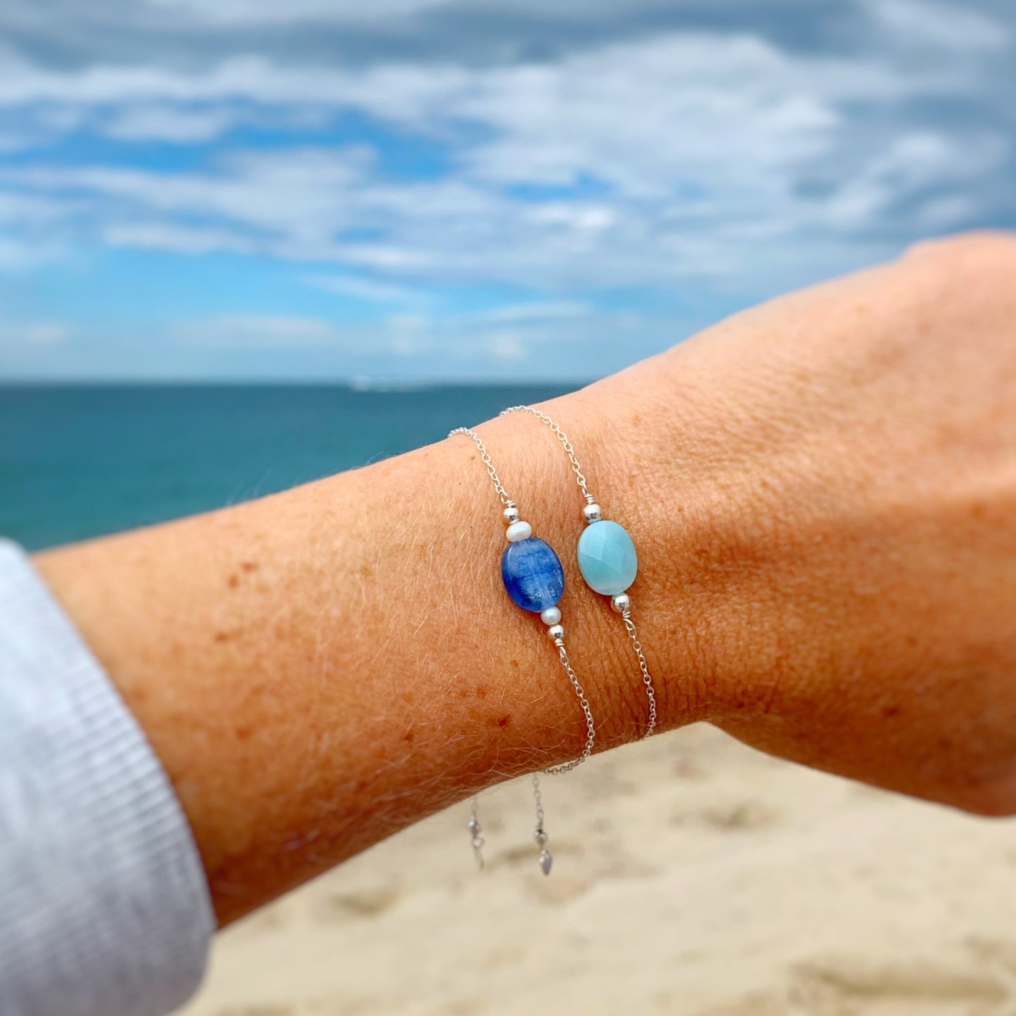 image of 2 bracelets close up stacked on a wrist. the first bracelet is the brewster bracelet and the second is the laguna bracelet. the background in this photo is a soft blurry beach scene