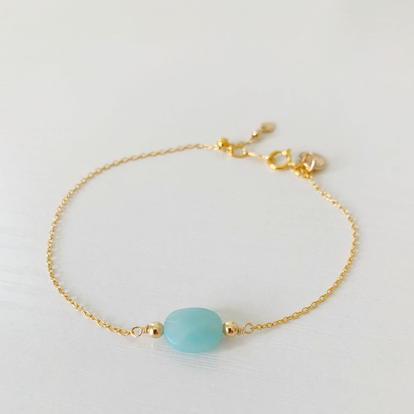 the Laguna adjustable bracelet by mermaids and madeleines is an adjustable 14k gold filled chain bracelet with a slide bead at the clasp and an oval faceted amazonite bead at the center of the bracelet. this piece is photographed flat on a white surface