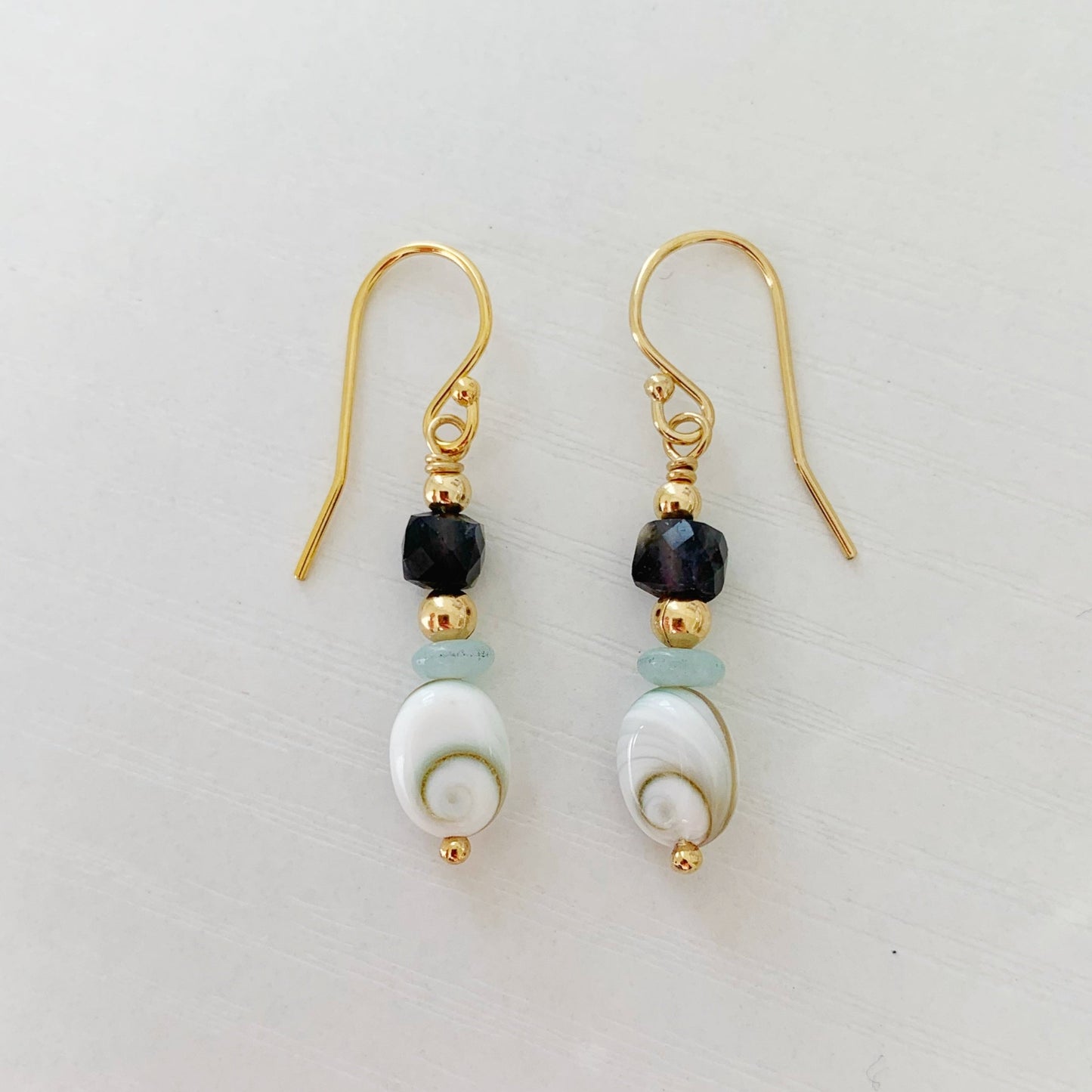 Mermaid Money earrings by mermaids and madeleines are designed with shiva shell oval beads complimented with small amazonite disc beads and iolite faceted cubes with 14k gold filled beads and findings. this pair is photographed on a white backgorund