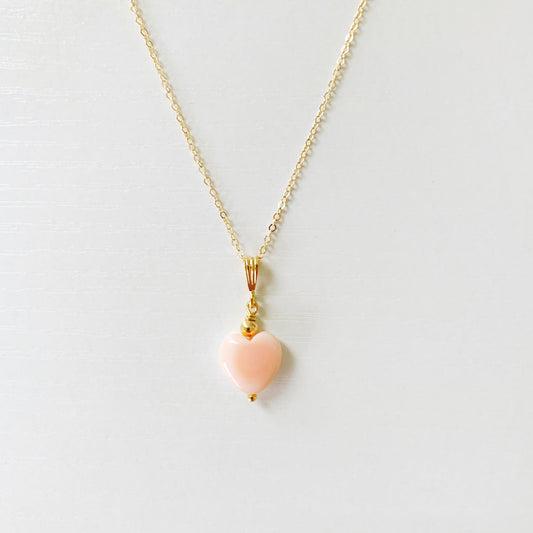 the pink posy necklace by mermaids and madeleines is a pendant style necklace on a 14k gold filled cable chain with length options of 16" or 18" and the pendant is a pink heart shaped conch shell. this necklace is photographed flat on a white surface with the front half of the necklace in view