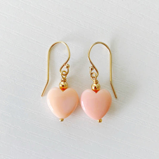 the pink posy earrings by mermaids and madeleines are simple drop earrings created with 14k gold beads and findings and feature a conch shells carved into hearts. this pair is photographed on a white surface