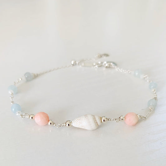 the seersucker shellebration bracelet by mermaids and madeleines is a sterling silver and beaded adjustable bracelet with a shell and coral beads at the center complimented by alternating aquamarine and moonstone. this bracelet is photographed on a white surface