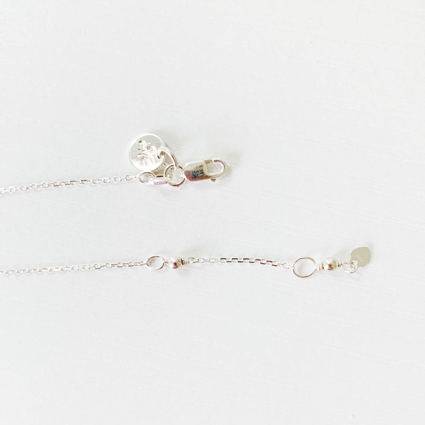 Image is a picture of a close up view of the back of the Truro necklace showing the sterling silver chain, clasp and the closure loop that is at 17" and 18" all photographed on a white surface