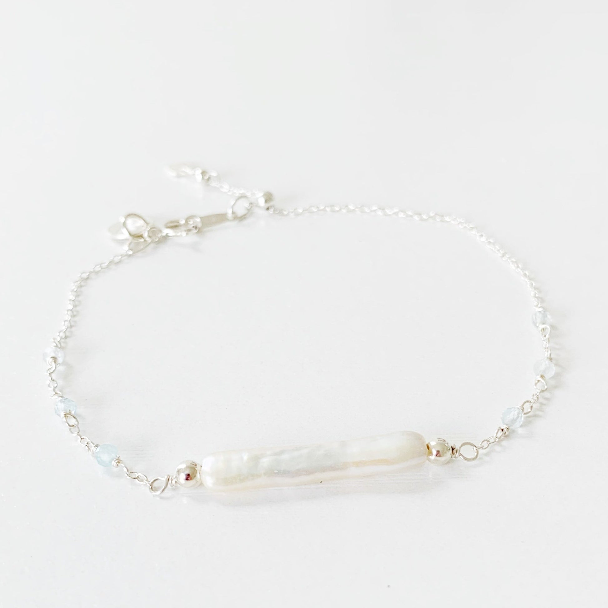 the Truro Adjustable bracelet by mermaids and madeleines features a freshwater stick pearl at the center with small microfaceted aquamarine beads on either side on the chain. the chain, findings and slide bead at the clasp are all made of sterling silver. this bracelet is photographed on a white surface