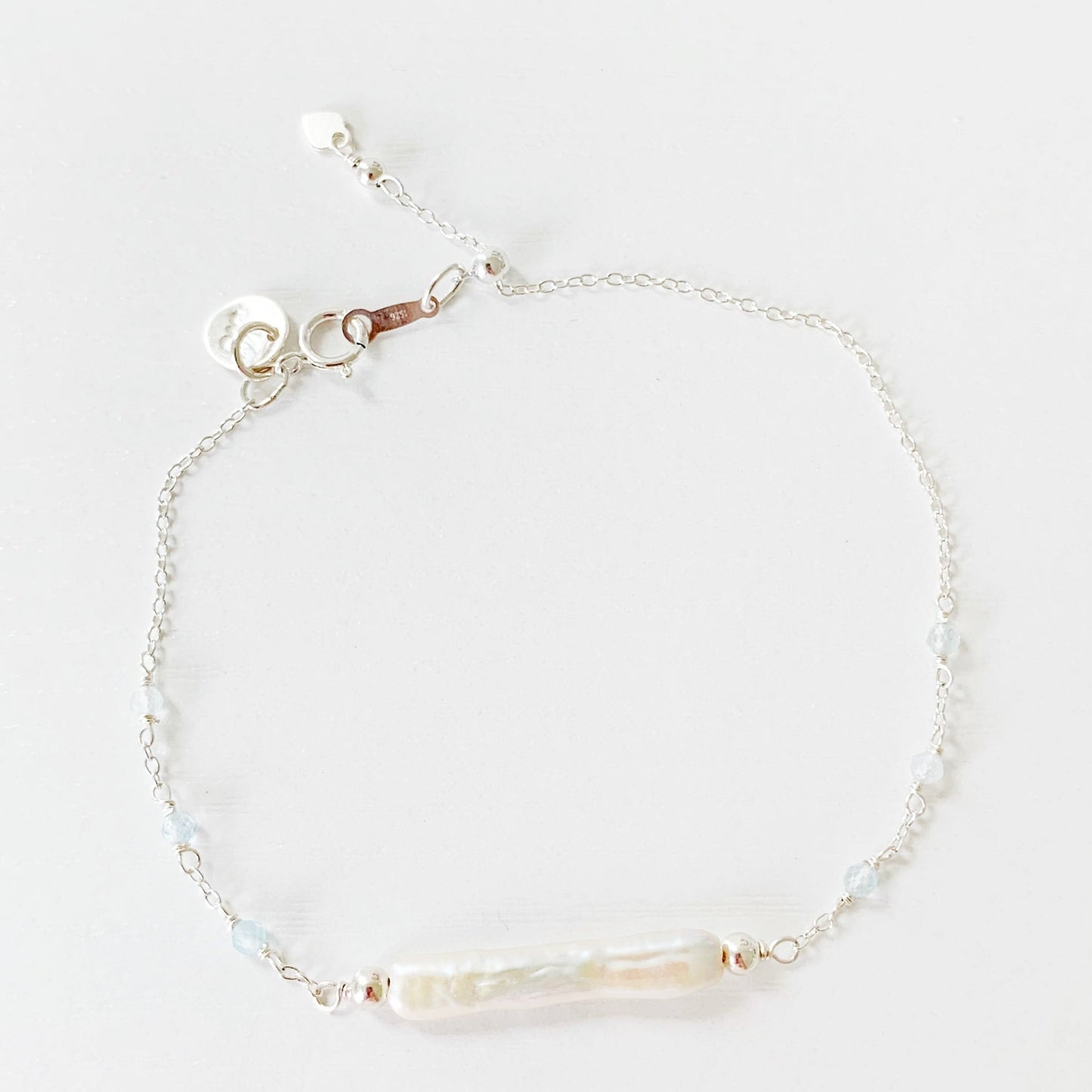 the Truro Adjustable bracelet by mermaids and madeleines features a freshwater stick pearl at the center with small microfaceted aquamarine beads on either side on the chain. the chain, findings and slide bead at the clasp are all made of sterling silver. this bracelet is photographed on a white surface