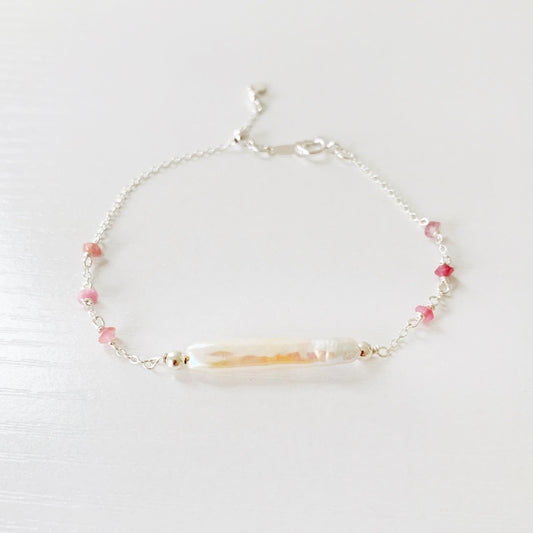 the pink azalea adjustable bracelet by mermaids and madeleines is a sterling silver chain bracelet with a slide bead near the closure. the center of the bracelet features a freshwater pearl bar and it has small pink tourmaline beads on the sides of the chain. this bracelet is photographed on a white surface with a front view