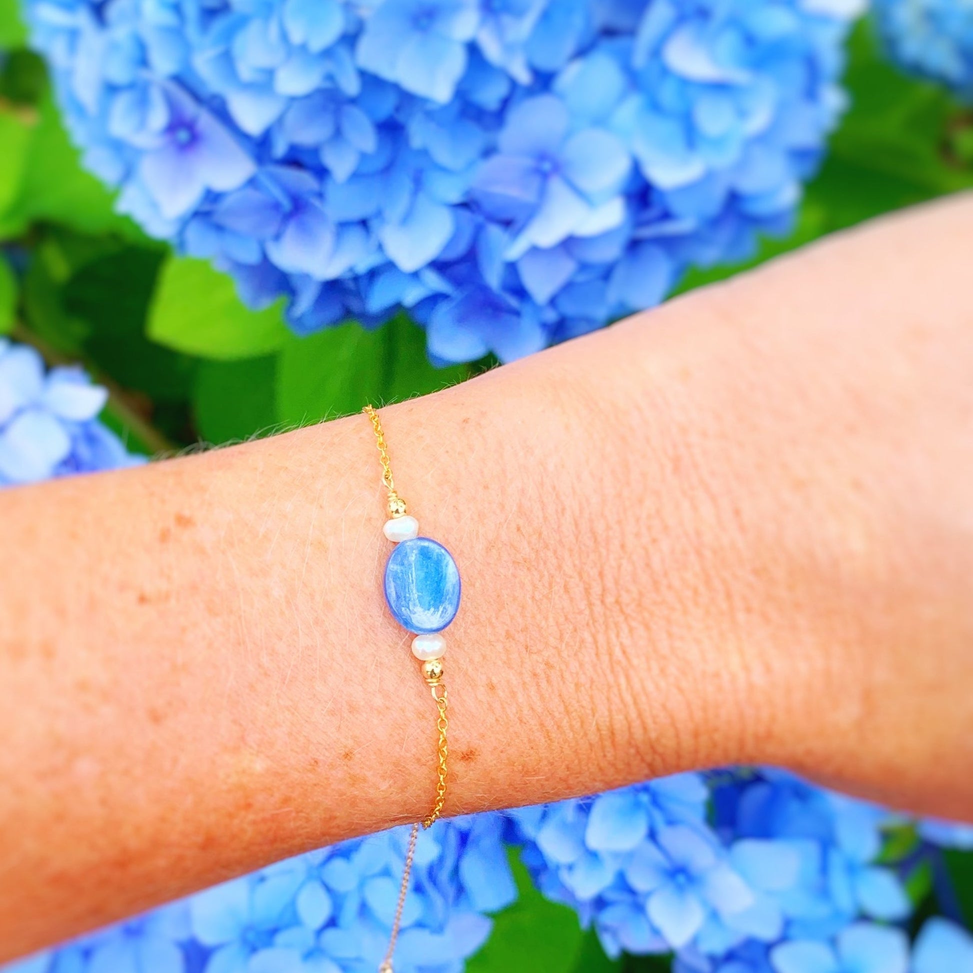 brewster adjustable bracelet by mermaids and madeleines is a gold filled chain bracelet with a slide bead at the clasp and a blue kyanite gem with freshwater pearls on either side as the focal point at the center