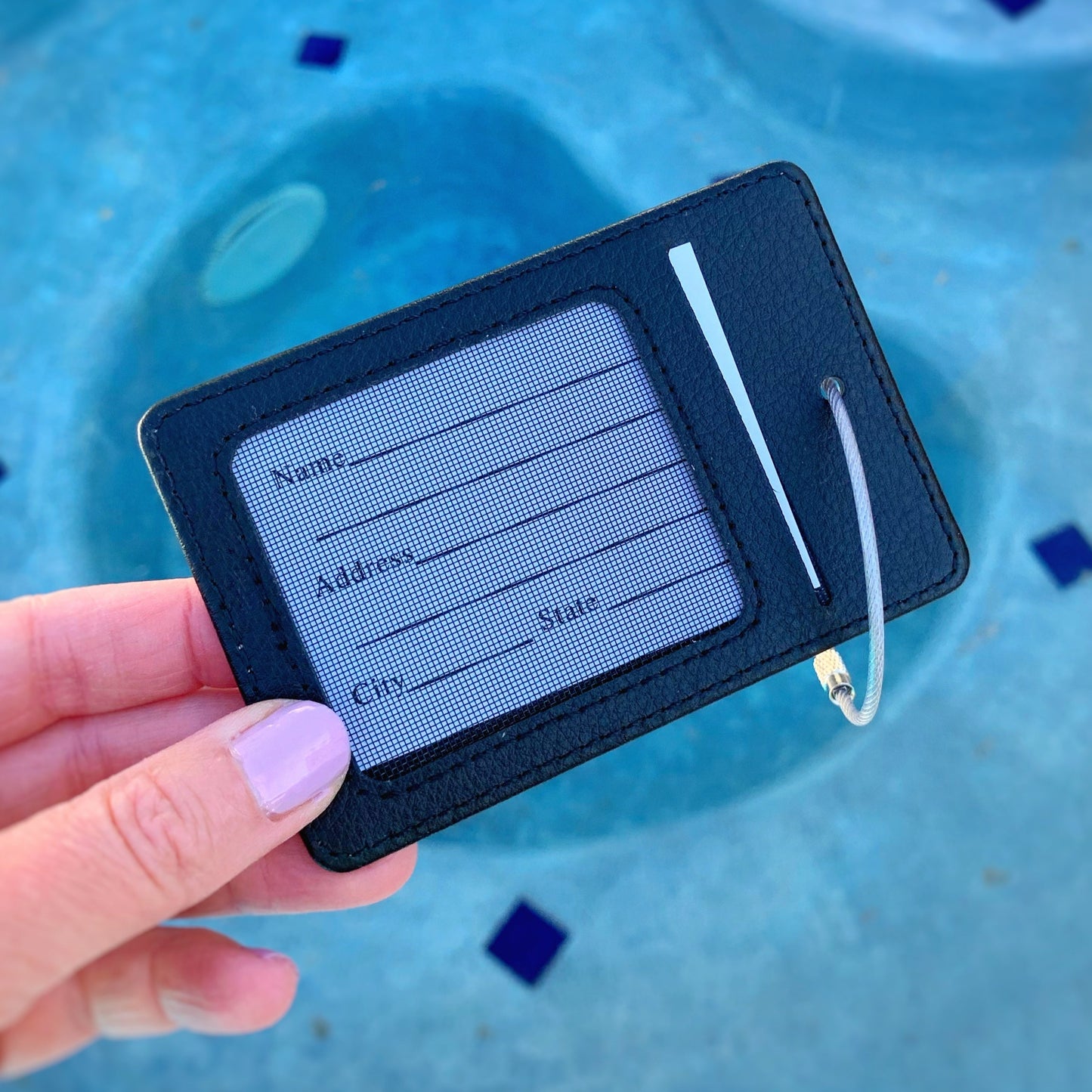 this is an image of the back of the flamingal luggage tag. this tag is held up in a hand with a blue pool in the background