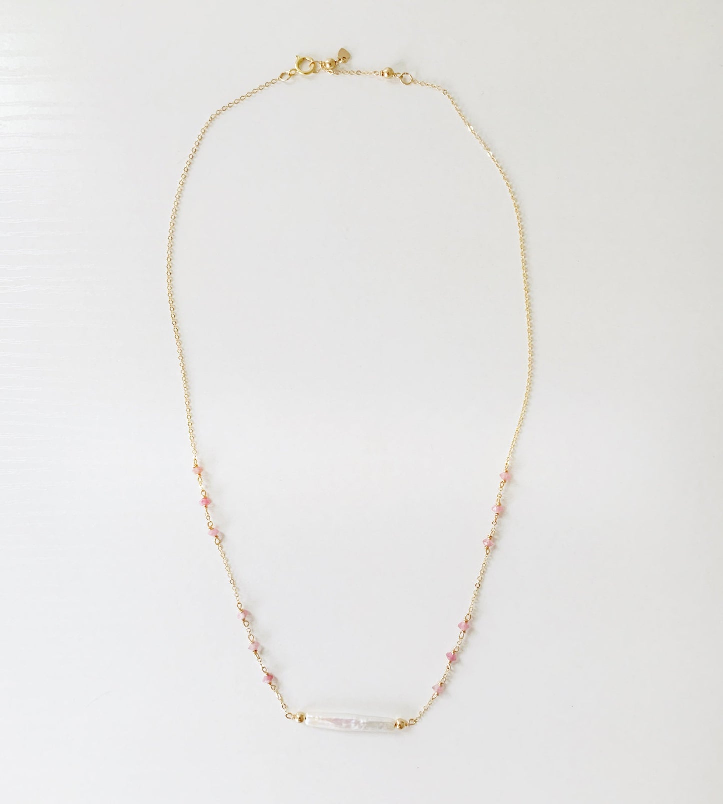 the pink azalea necklace by mermaids and madeleines is a freshwater pearl bar necklace with pink tourmaline faceted beads in groups of 3 on the 14k gold filled chain. this necklace is photographed in full on a white surface