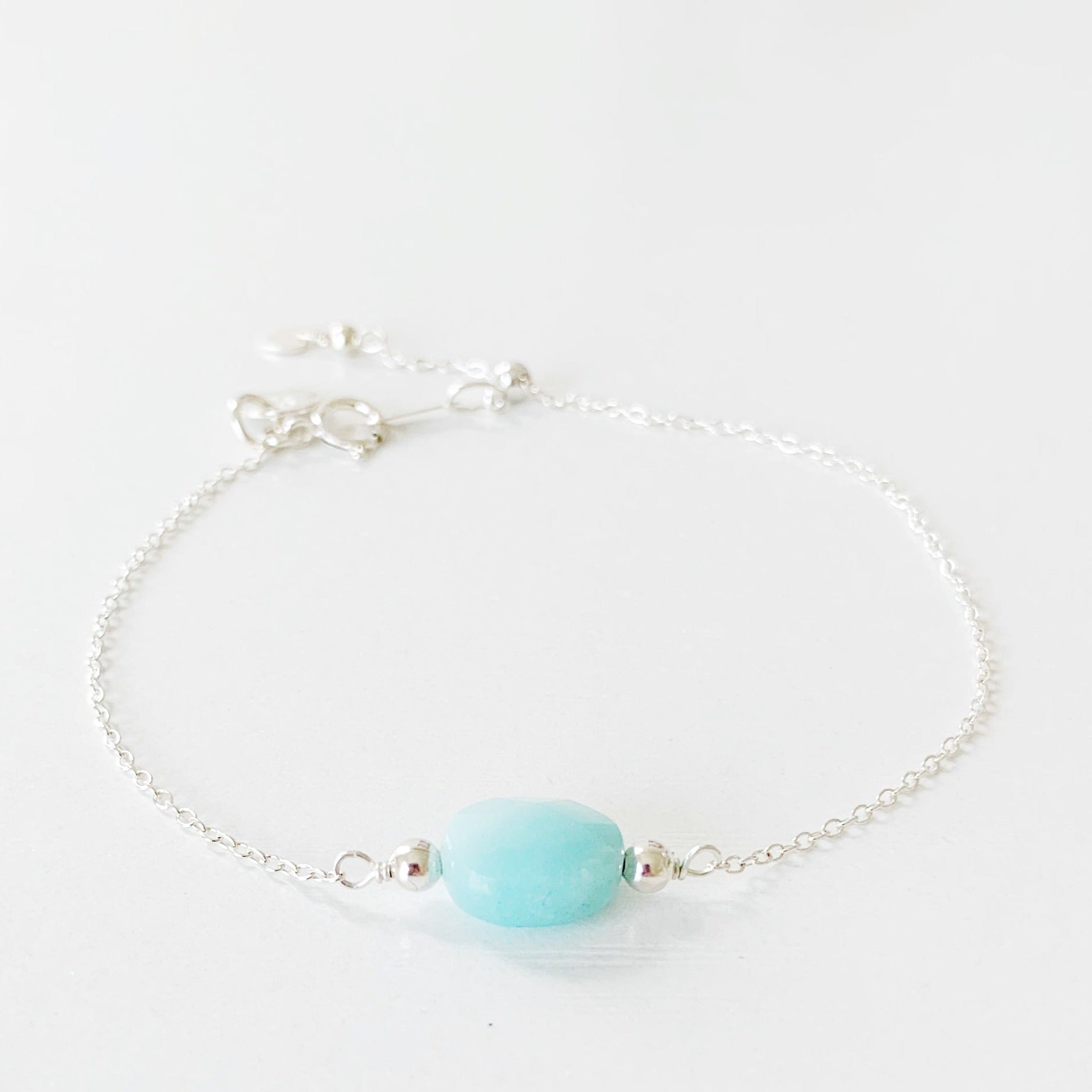 the mermaids and madeleines bracelet is a sterling silver chain bracelet with a faceted amazonite oval shaped bead at the center and a slide bead near the clasp to make it adjustable. this bracelet is photographed on a white surface