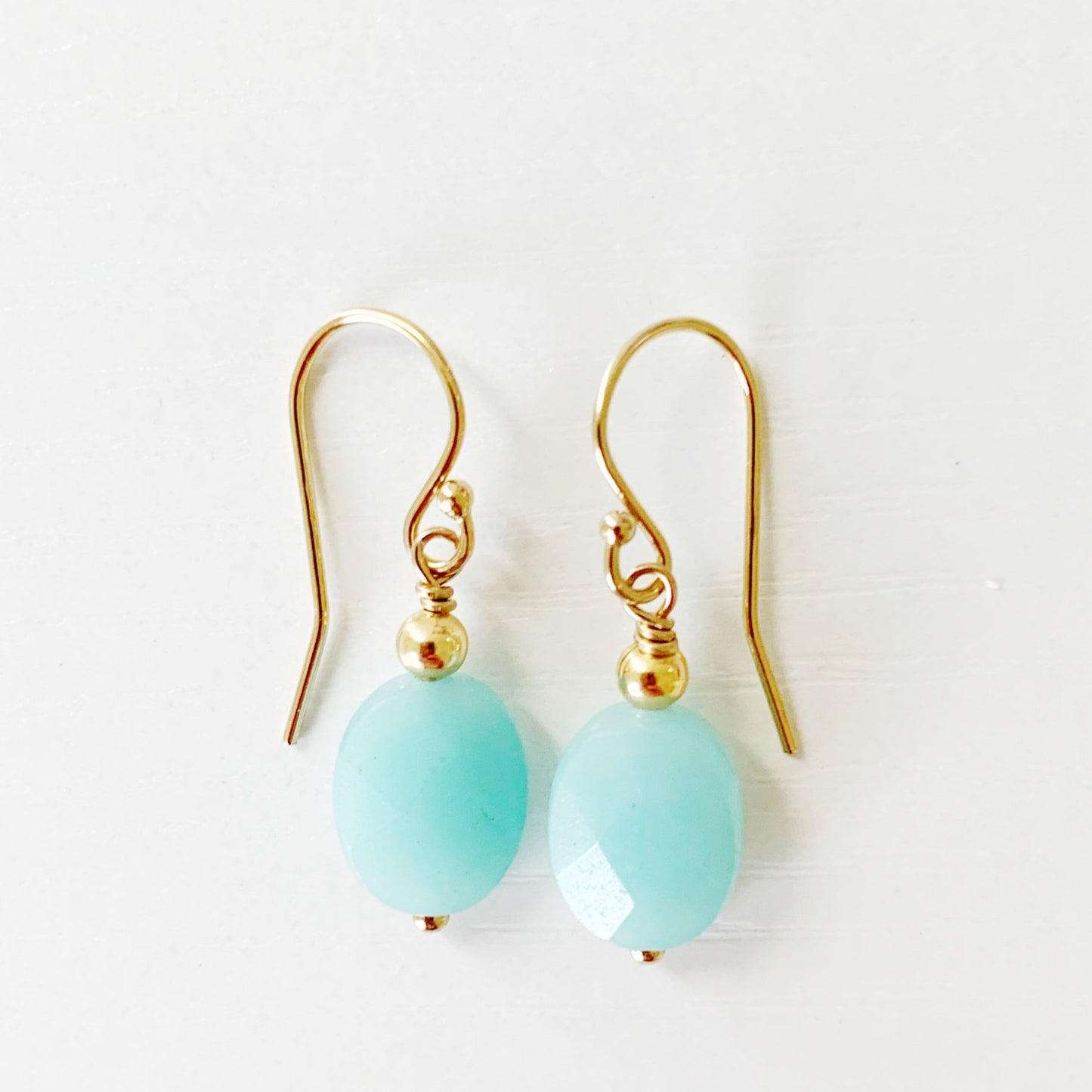 the mermaids  and madeleines laguna earrings are simple drop style earrings designed with faceted oval amazonite beads dropped from 14k gold filled earring findings. this pair is photographed flat on a white surface