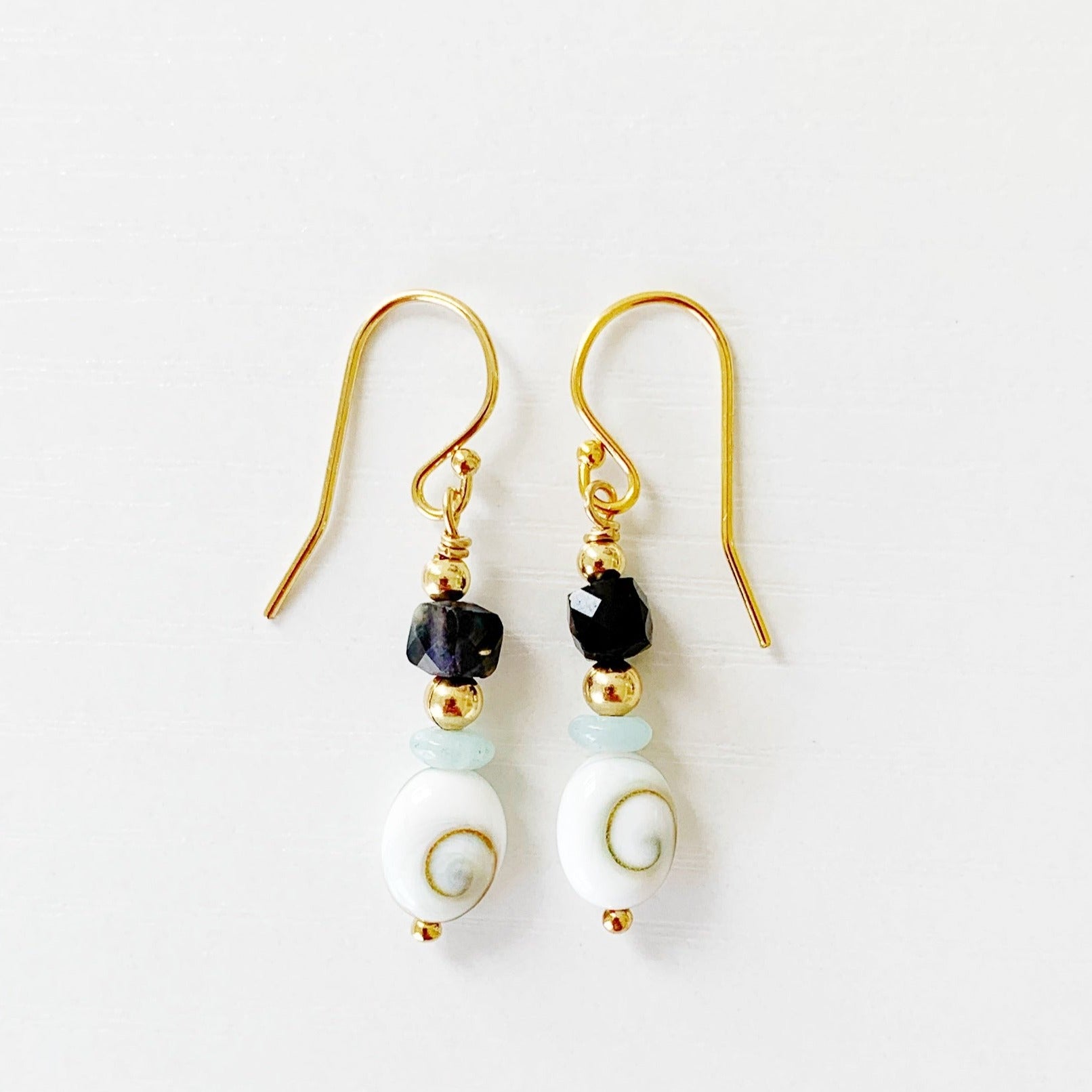 mermaid money earrings by mermaids and madeleines are designed with shiva shells, iolite and amazonite beads. this pair is photographed on a white surface