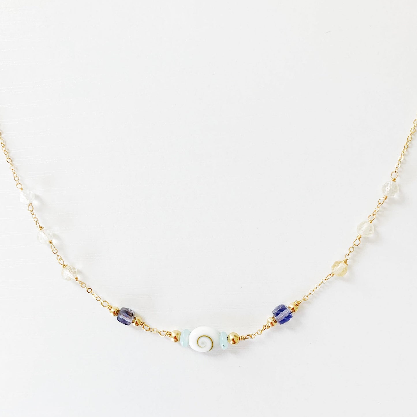 the mermaid money necklace by mermaids and madeleines is a 14k gold filled chain necklace with beads throughout and a shiva shell at the center. this necklace is photographed with the front half and on a white surface