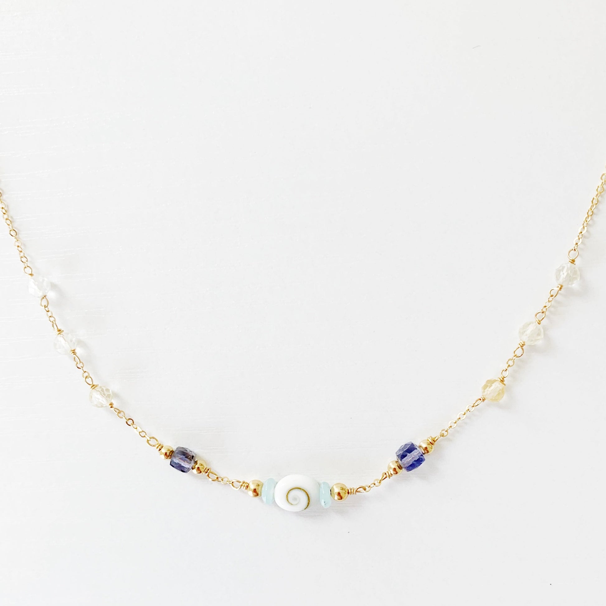 the mermaid money necklace by mermaids and madeleines is a 14k gold filled chain necklace with beads throughout and a shiva shell at the center. this necklace is photographed with the front half and on a white surface