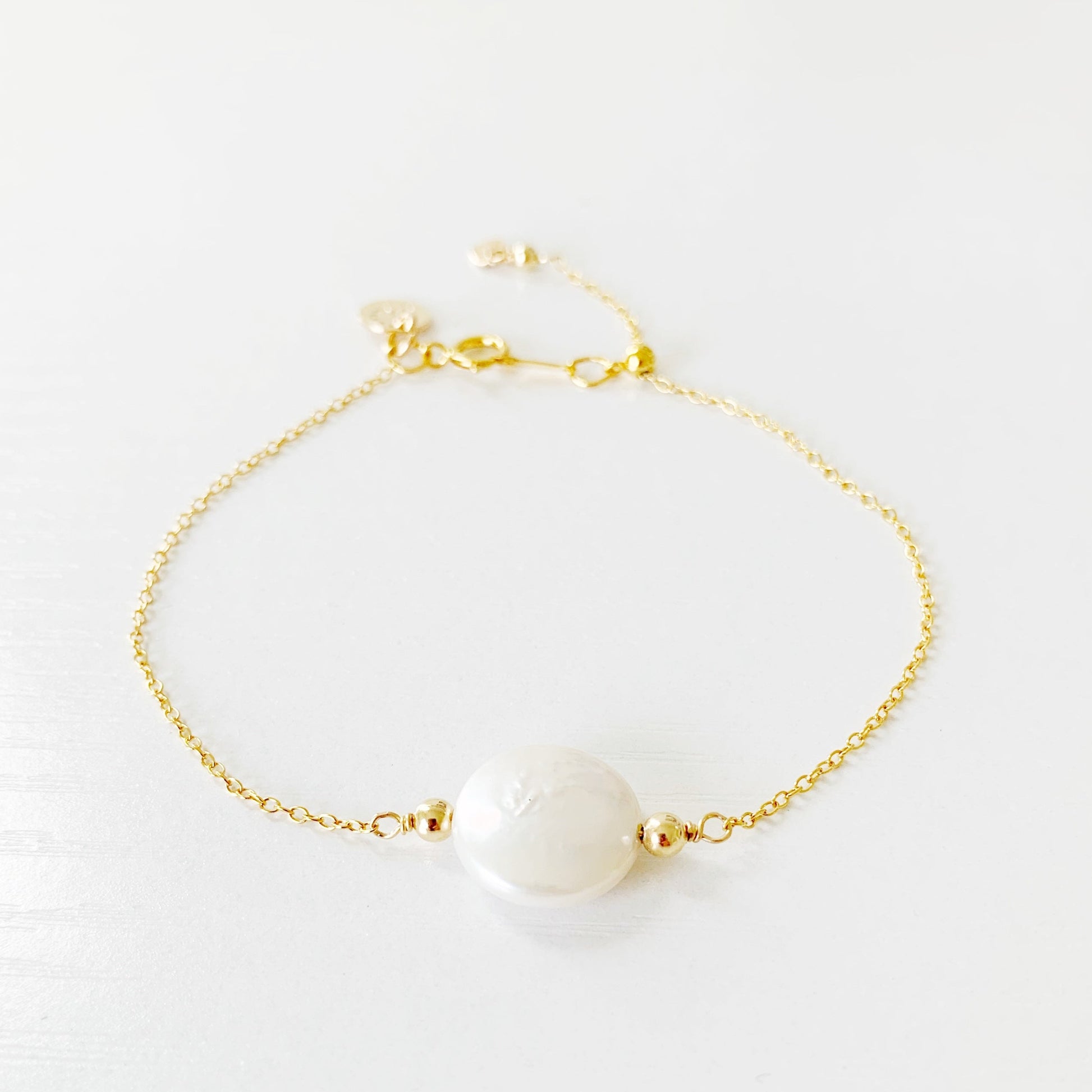 the newport bracelet by mermaids and madeleines is a chain bracelet with a freshwater coin pearl at the center on a 14k gold filled chain with a slide bead near the clasp. this bracelet is photographed on a white surface