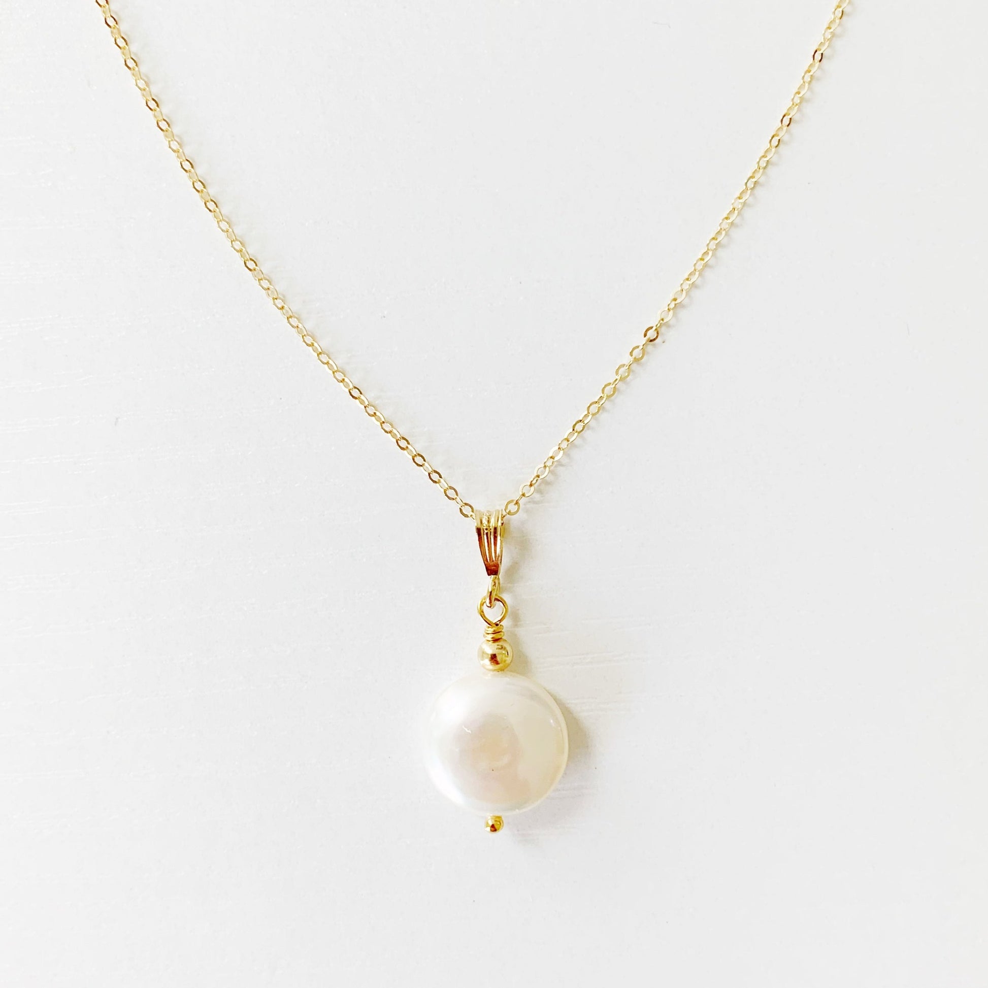 the newport necklace by mermaids and madeleines is a freshwater coin pearl suspended from a 14k gold filled chain and findings. this necklace is photographed on a white surface