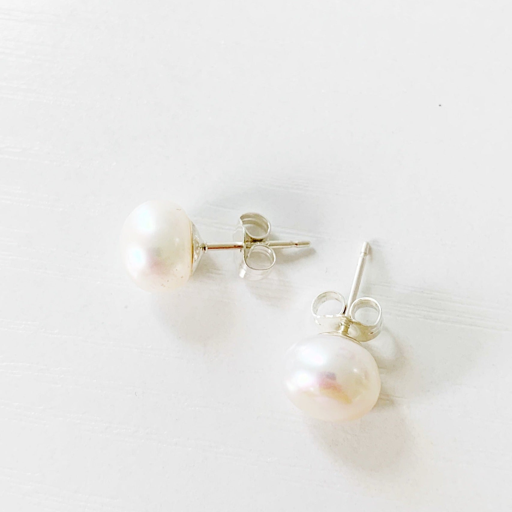 the pearlfect day earrings by mermaids and madeleines are freshwater button pearl earring studs with sterling silver findings. this pair is photographed from a top view and they're on a white surface