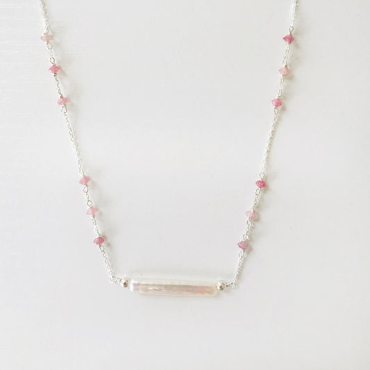 the pink azalea necklace by mermaids and madeleines is a sterling silver chain necklace with a freshwater pearl bar at the center and small pink tourmaline beads in groups of 3 going up the sides of the chain. this necklace is photographed on a white surface with the front half of the necklace in view