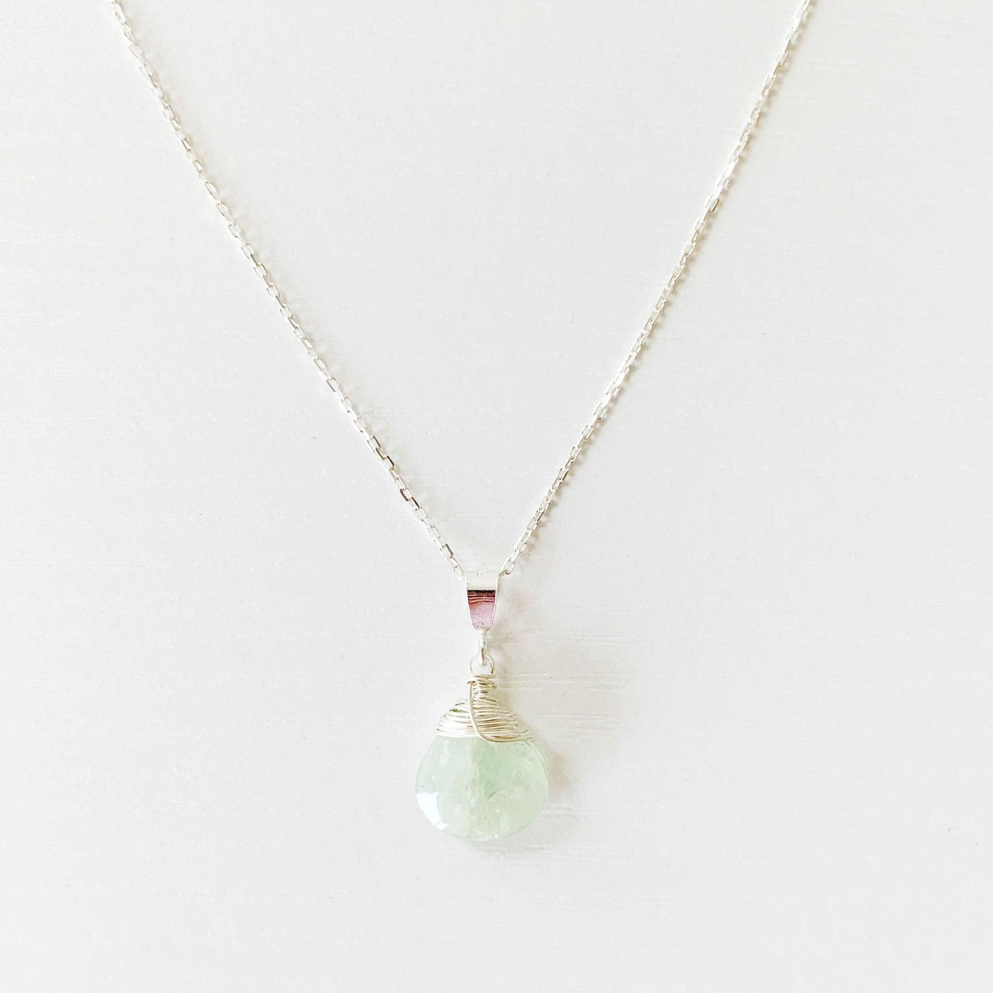 the raindrop necklace by mermaids and madeleines is a faceted briolette of aquamarine wire wrapped with sterling silver and hanging from a sterling silver chain with findings. this image is the front part of the necklace photographed on a white surface