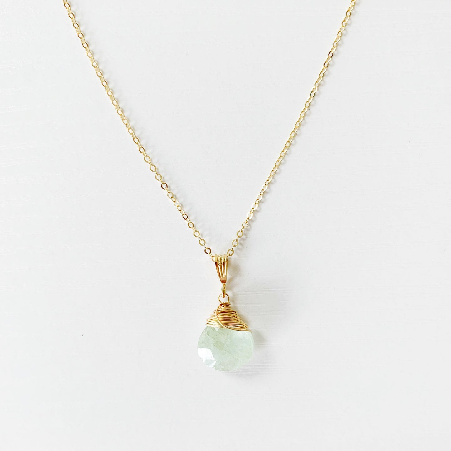 the raindrop pendant necklace by mermaids and madeleines is a aquamarine faceted briolette wire wrapped with 14k gold filled wire and suspended from 14k gold filled chain with findings. this is a close up image of the front section of the necklace on a white surface