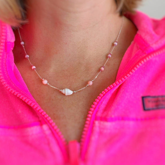 an image of the pink lemonade shellebration necklace on a person's neck that's wearing a bright pink zip up top.