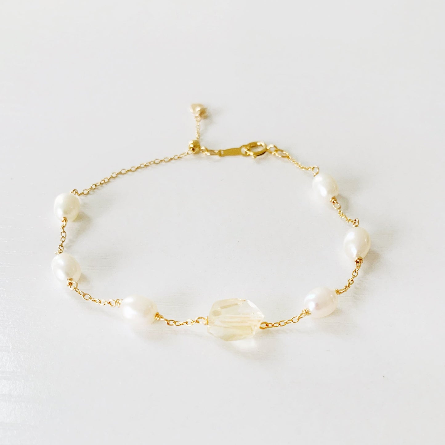 The sun and snow bracelet by mermaids and madeleines is an adjustable 14k gold filled chain bracelet with a slide bead at the clasp. the bracelet features a light yellow faceted citrine gem at the center with freshwater rice shaped pearls going up the sides. this bracelet is photographed flat on a  white surface