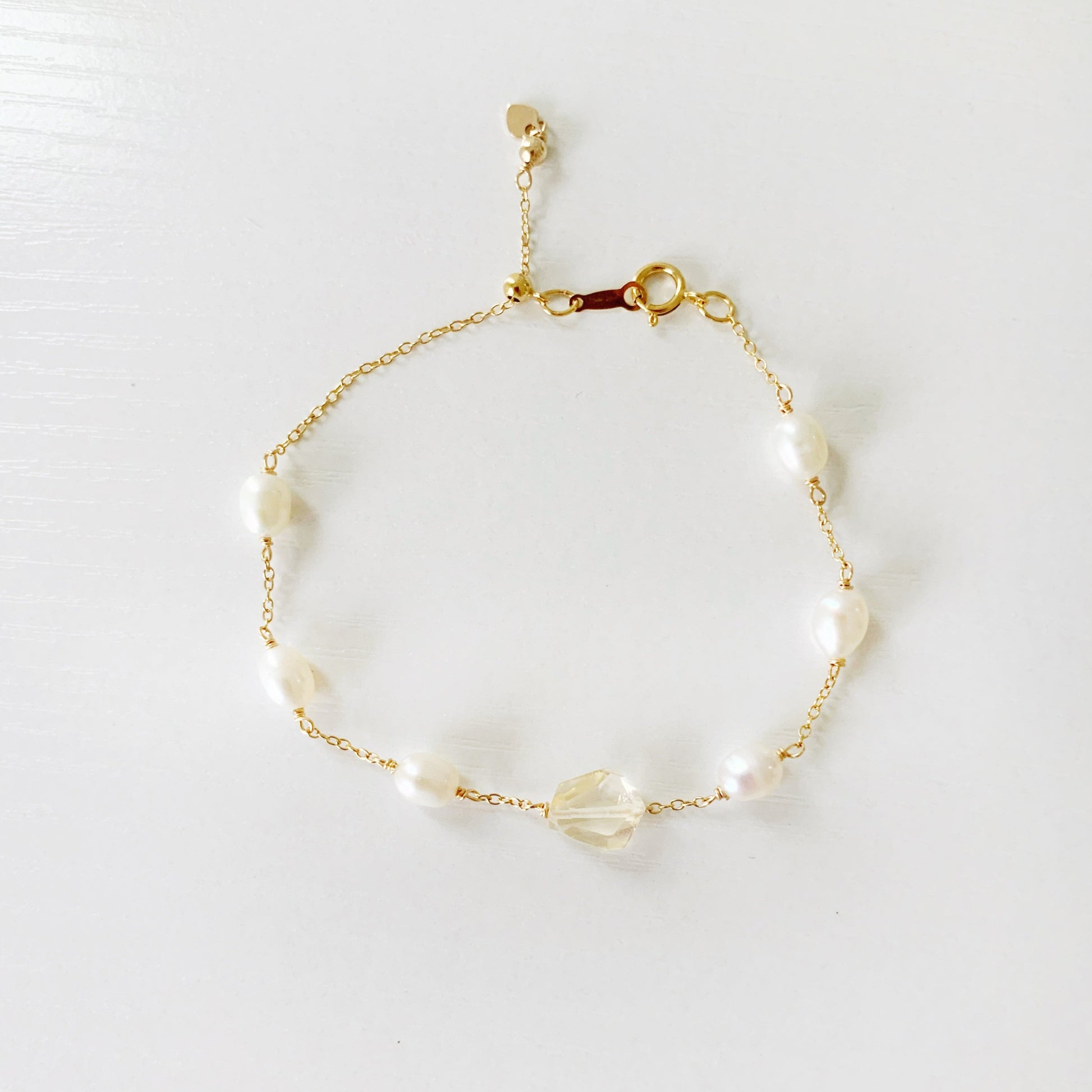 The sun and snow bracelet by mermaids and madeleines is an adjustable 14k gold filled chain bracelet with a slide bead at the clasp. the bracelet features a light yellow faceted citrine gem at the center with freshwater rice shaped pearls going up the sides. this bracelet is photographed flat on a  white surface with a top down view