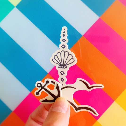 temporary tattoos designed by mermaids and madeleines. there are 3 designs here. A mini anchor, an artsy shell and seagull silhouettes. this is an image of one of each temporary tattoo design being held up in a hand with a vibrant striped background