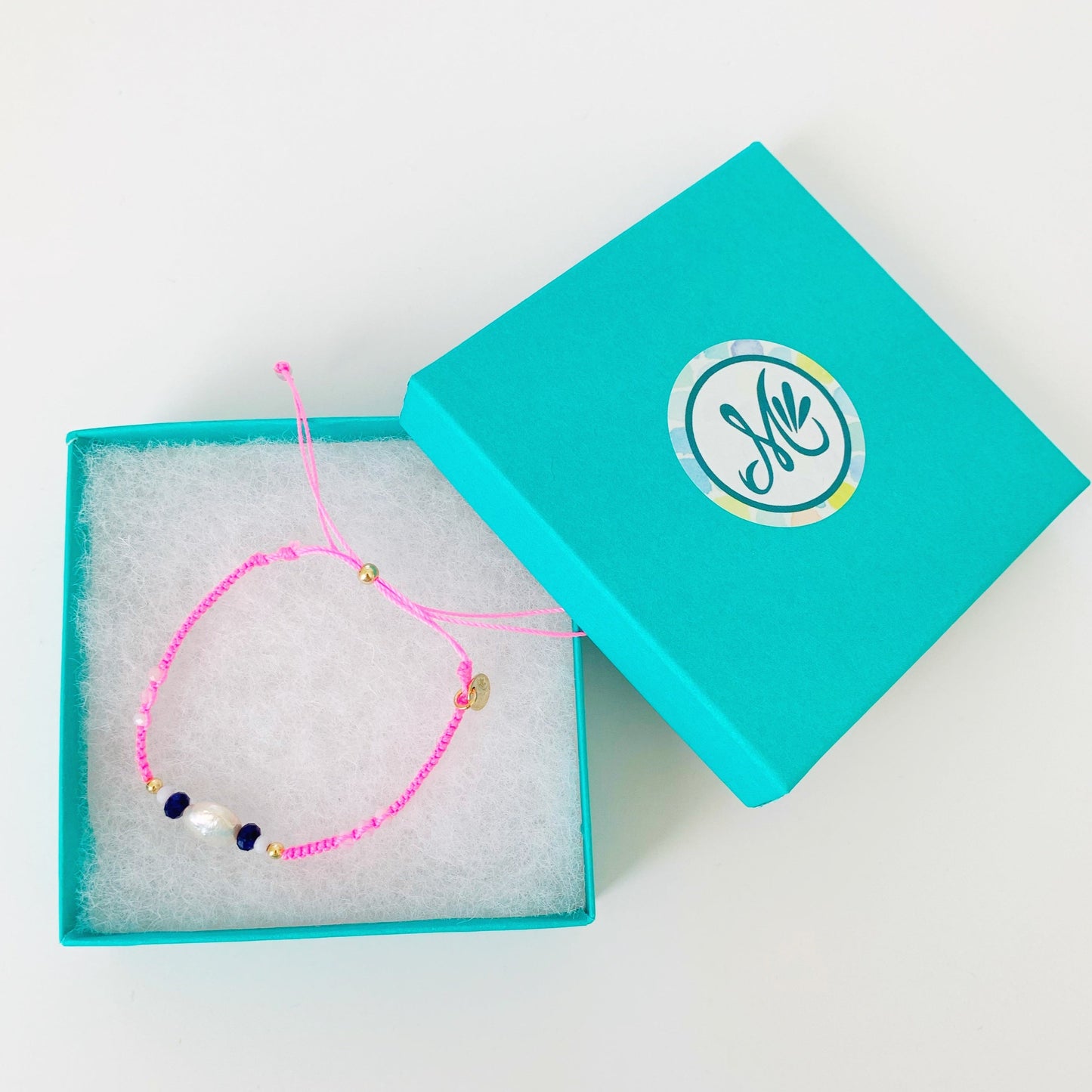 neon pink macrame bracelet pictured in a teal mermaids and madeleines gift box on a white surface