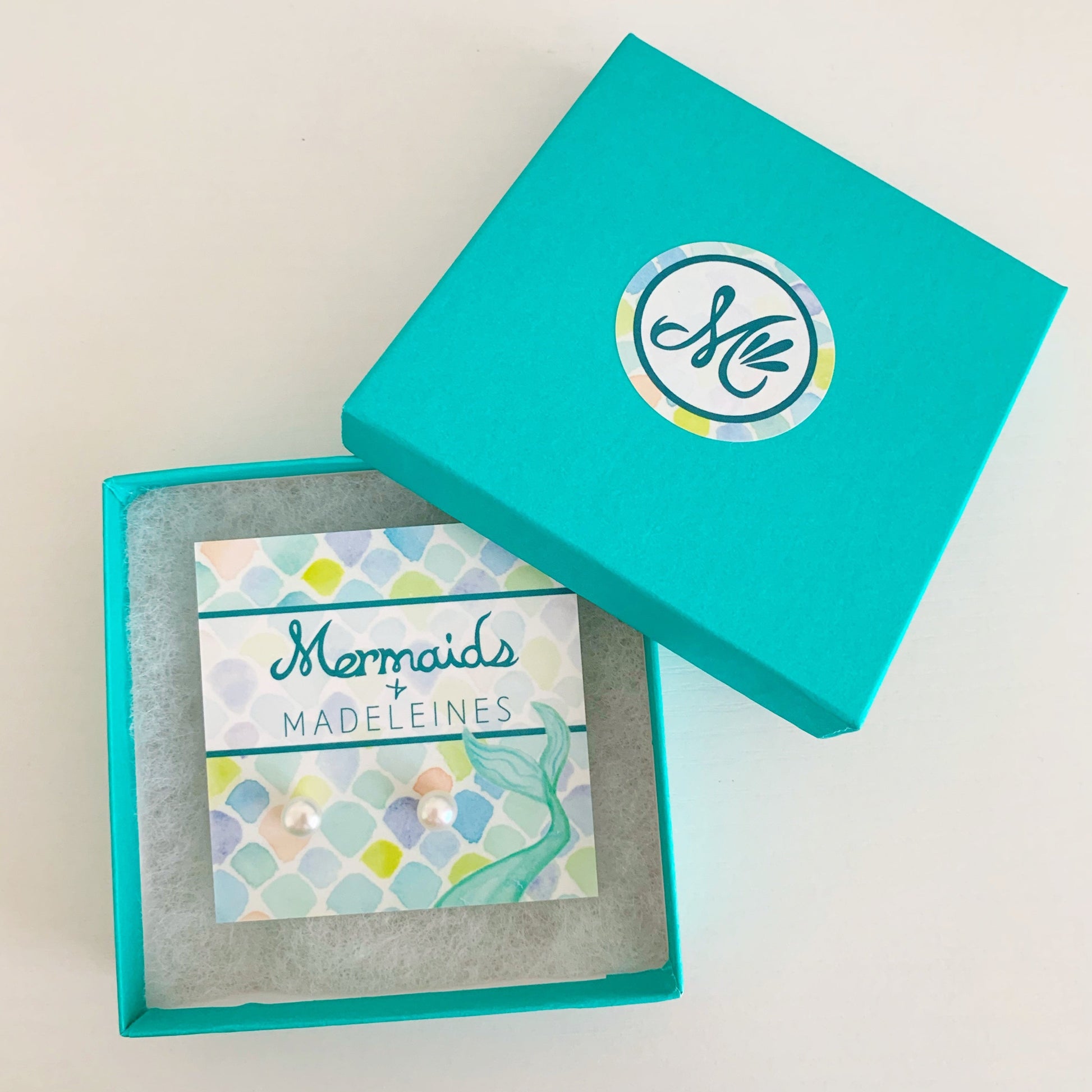 Pearlfect Day pearl earrings by mermaids and madeleines feature freshwater button pearls on sterling silver posts. this pair is placed on a branded card and set into a cotton lined teal gift box on a white surface