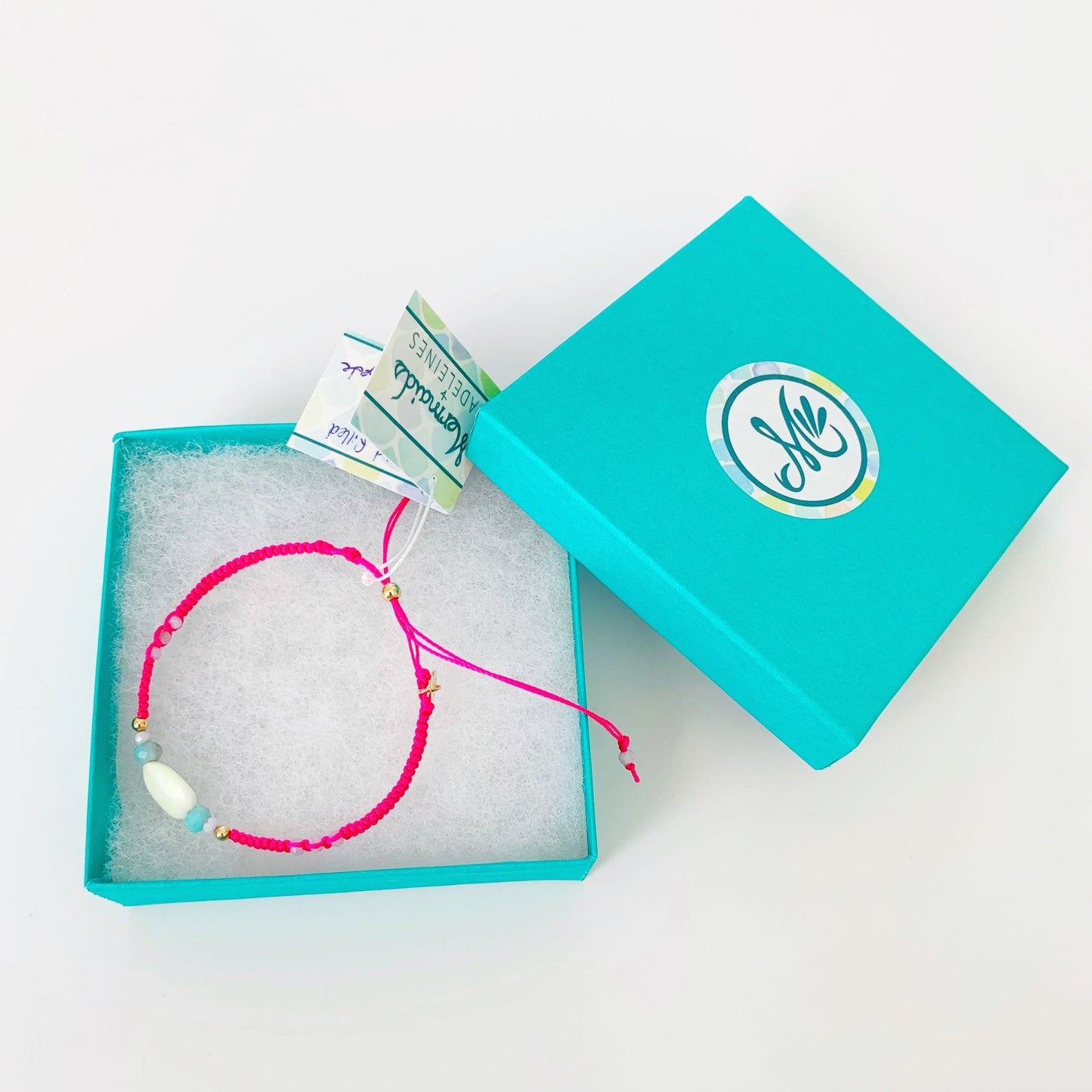 Pink macrame bracelet with semiprecious beads pictured in a teal gift box on a white table